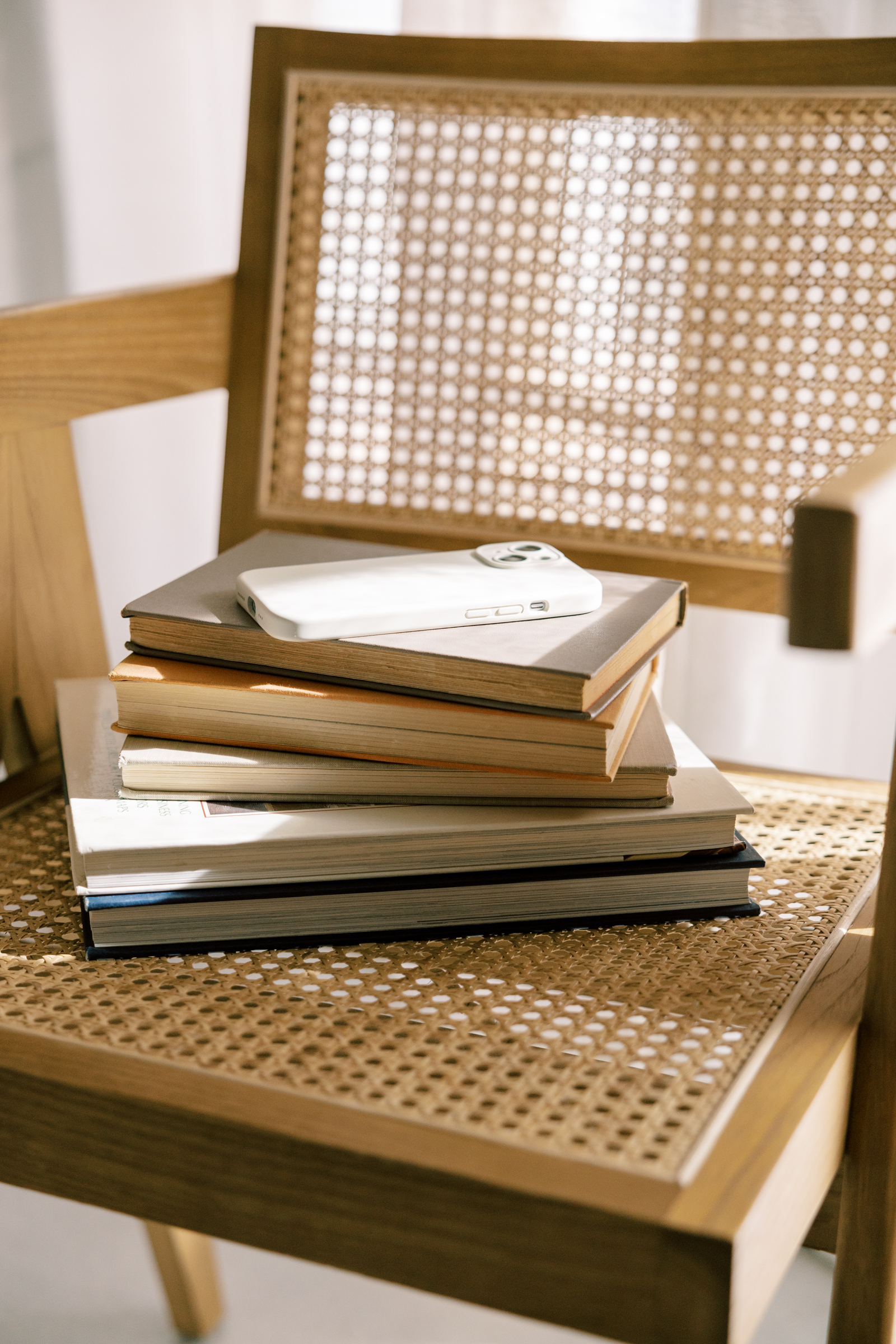 Stack of books and a smartphone on a woven wooden chair in natural light